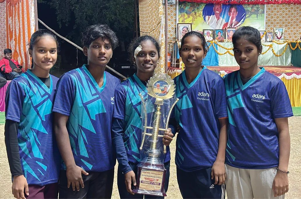 Five young women in Adani Foundation jerseys holding a kabaddi first-prize trophy