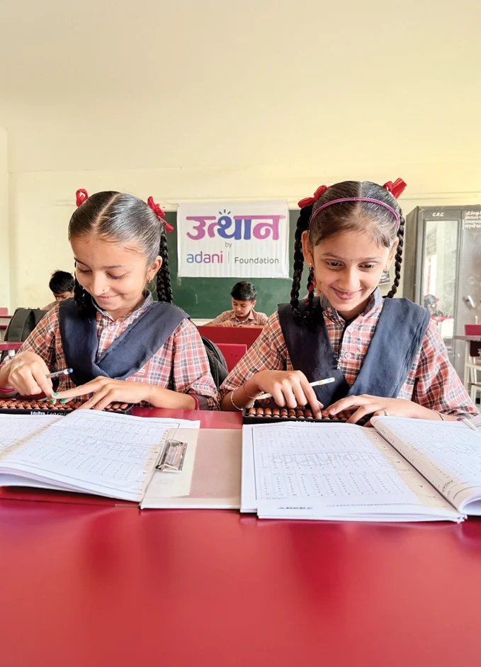 Two schoolgirls using abacuses beneath an Utthan by Adani Foundation banner