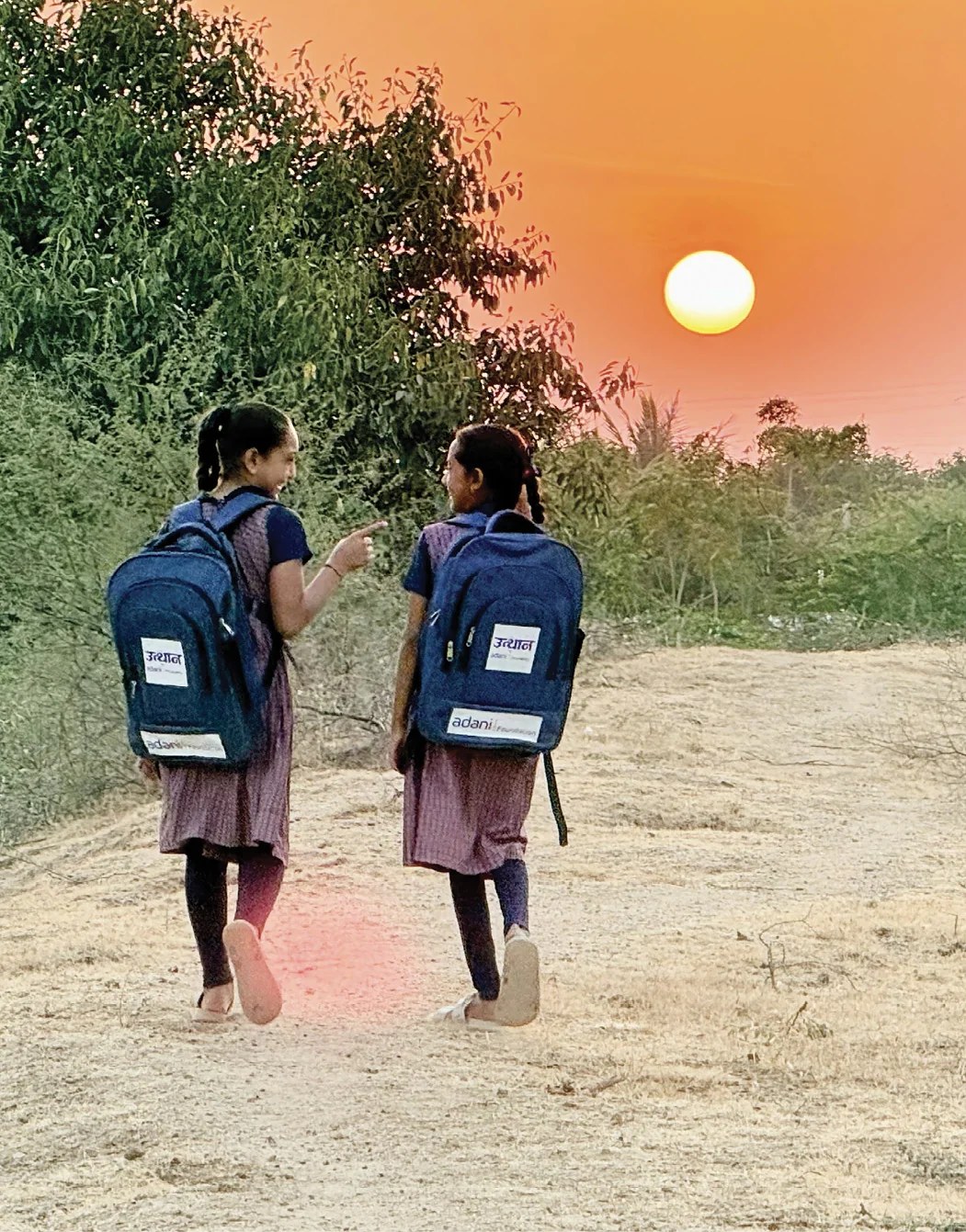 Two schoolgirls with Adani Foundation Utthan backpacks walking home at sunset